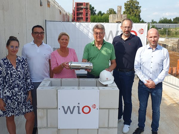 Eine Zeitkapsel im WiO-Neubau im Osnabrücker Landwehrviertel versenkten jetzt (v.l.n.r.) Lena-Marie Berg (Leiterin WiO-Immobilienmanagement), Wigand Maethner (WiO-Geschäftsführer), Susanne Hambürger dos Reis (WiO-Aufsichtsratsvorsitzende), Dr. E.h. Fritz Brickwedde (Stellvertr. WiO-Aufsichtsratsvorsitzender), Holger Clodius (WiO-Geschäftsführer) und Marco Lange (Leiter Immobilienentwicklung).