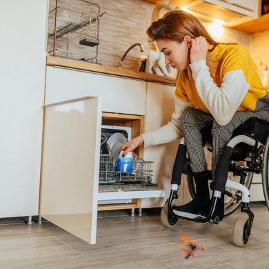 Eine Frau im Rollstuhl, die zu Hause einen Geschirrspüler benutzt. Foto: bernardbodo – stock.adobe.com